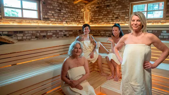 Vier Frauen stehen in der Sauna umhüllt von Saunatüchern