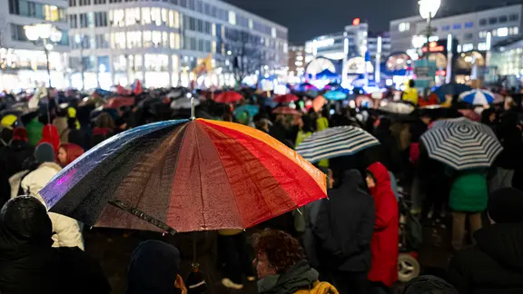Zahlreiche Menschen nehmen mit bunten Regenschirmen an einer Demonstration zur Migrationspolitik auf dem Opernplatz in der Innenstadt teil.