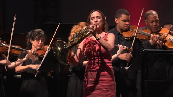 Die Hornistin Sarah Willis spielt auf der Bühne vor einem Orchester.