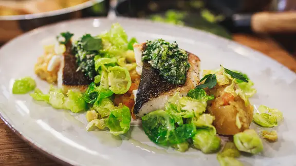 Skrei mit Rübenstampf und Rosenkohl auf einem Teller serviert.