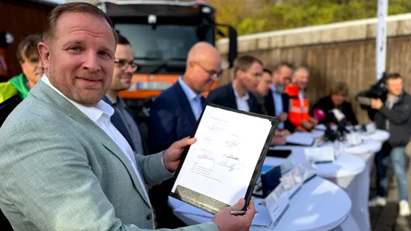 Bad Segebergs Bürgermeister Toni Köppen (parteilos) freut sich über die Einigung, die heute besiegelt wurde. | NDR, Tobias Gellert Bürgermeister Toni Köppen zeigt während der Pressekonferenz den Vertrag zum Bau der A20
