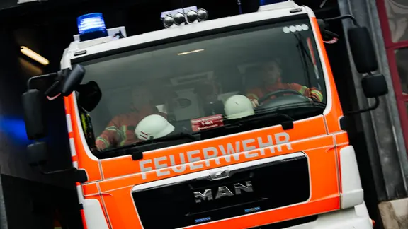 Ein Feuerwehrauto fährt mit Blaulicht aus einer Feuerwache heraus.