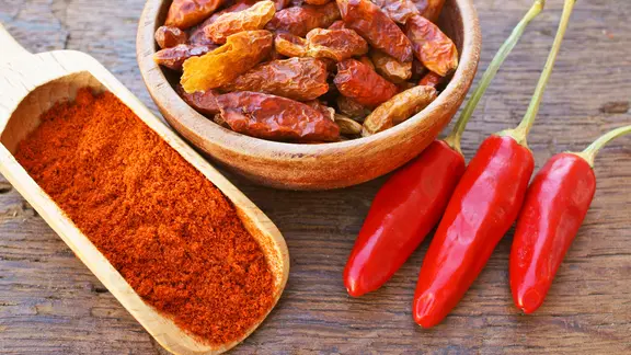 Frische rote Chilischoten, Chilipulver sowie getrocknete Chilischoten auf einem Holztisch.