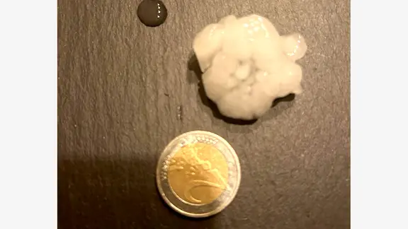 EIn Hagelkorn liegt neben einer Zwei-Euro-Münze.