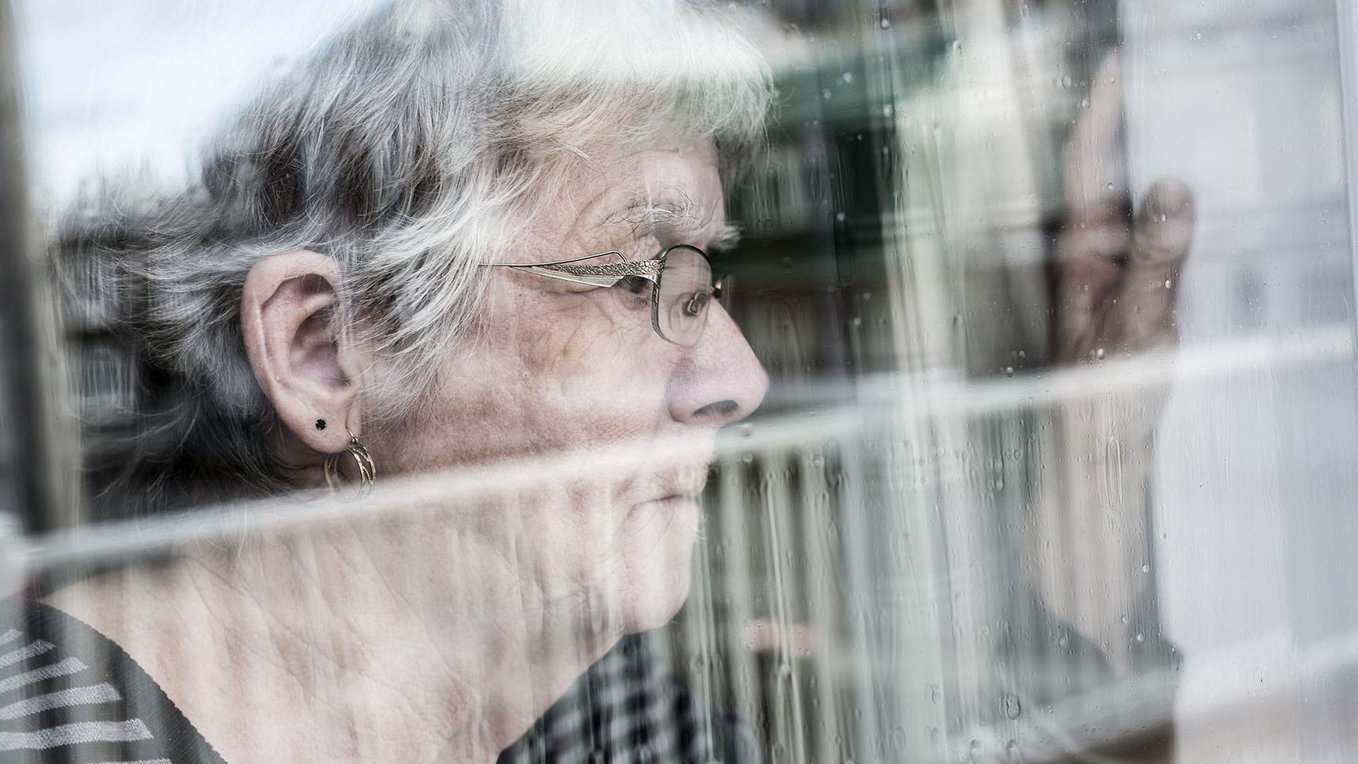 Eine ältere Frau schaut aus einem Fenster. | fotolia.com, pololia