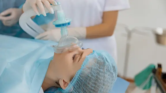 Eine Ärztin hält einer Patientin während einer OP eine Beatmungsmaske auf Mund und Nase.