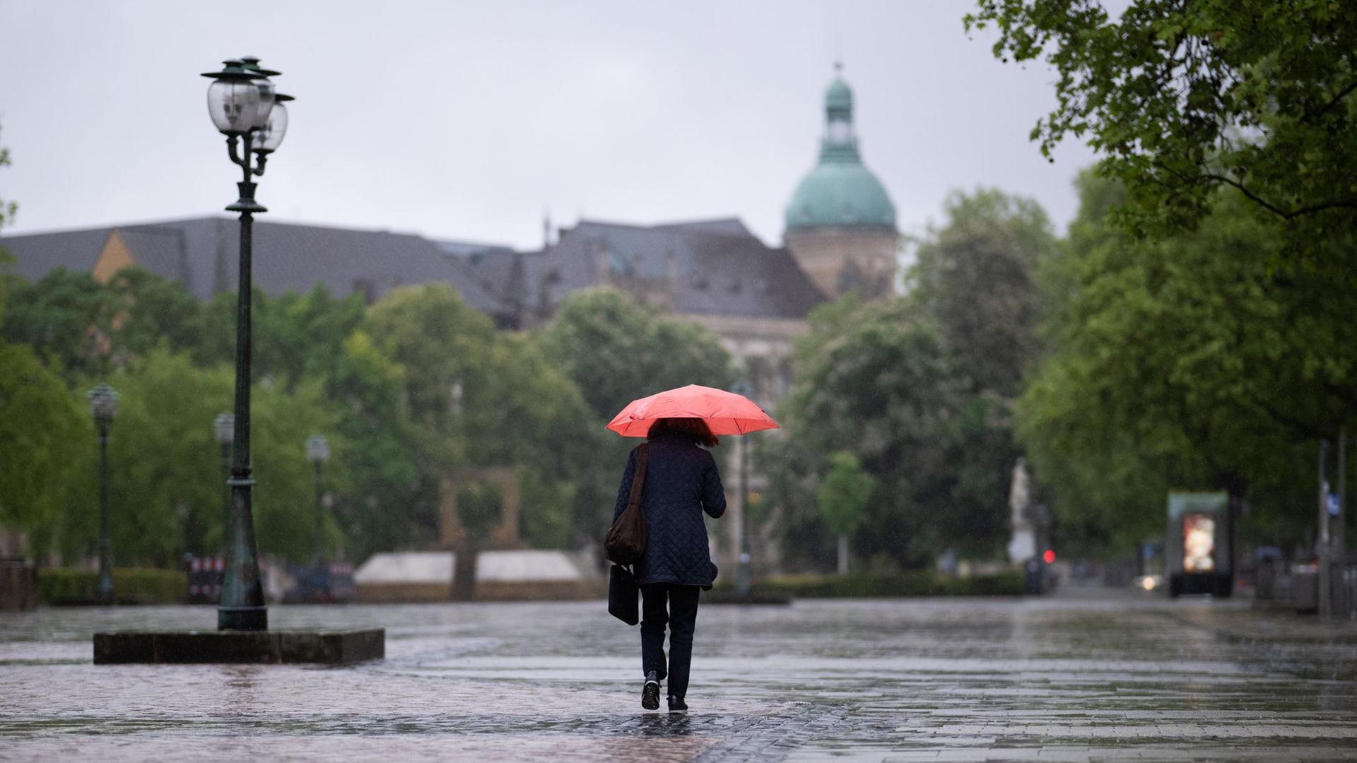 Niedersachsen, Hannover: Eine Frau läuft mit einem Regenschirm am frühen Morgen bei starken Regen durch die Innenstadt | dpa-Bildfunk, Julian Stratenschulte