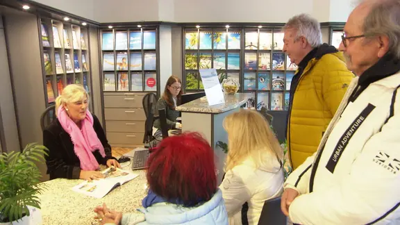 Mehrere Personen stehen in einem Reisebüro.