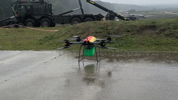 Bergen Wollgestelt Warden am Donnerstag Aus Kleinere Drohnen wie diese, die eine Kiste Transportieren cann. | НДР, Табеа Пандер Eine Drohne mit einer kleinen Kiste steht auf dem Boden.