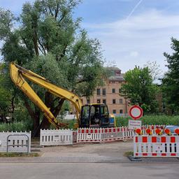 Auf dem Bild ist das Ende der Neuen Bleicherstraße zu sehen, an dem sich eine Baustelle befindet. Rot-weiße Absperrungen und ein Bagger sowie ein Lastanhänger stehen an dem Ufer des Seitenarmes der Warnow, bei dem die Fahrradbrücke gebaut werden soll. Die stelle befindet sich gegenüber dem Mühlendamm am Flussarm.