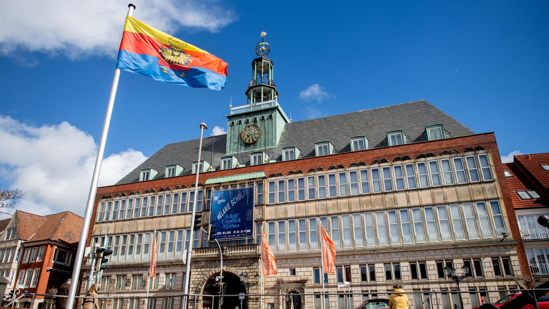 Eine Flagge mit dem Emder Stadtwappen weht bei sonnigem Wetter vor dem historischen Rathaus. | picture alliance/dpa, Hauke-Christian Dittrich