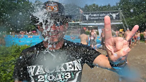 Wolfgang (52) aus Hessen zeigt am 01.08.2014 in Wacken (Schleswig-Holstein) im Schwimmbad unter einer Dusche die "Pommesgabel", den Gruß der Heavy-Metal Fans.