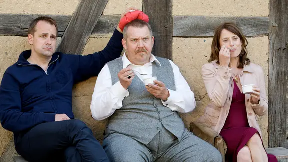 Klaus (Stephan Schad), Gilles (Dietmar Bär) und Marit (Inka Friedrich) sitzen auf einer Holzbank.