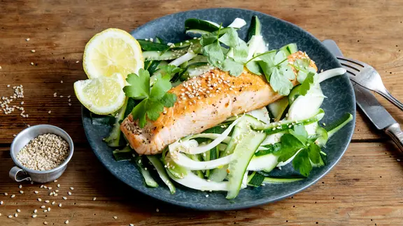 Ein Lachsfilet auf Gurken-Fenchel-Salat liegt auf einem Teller.