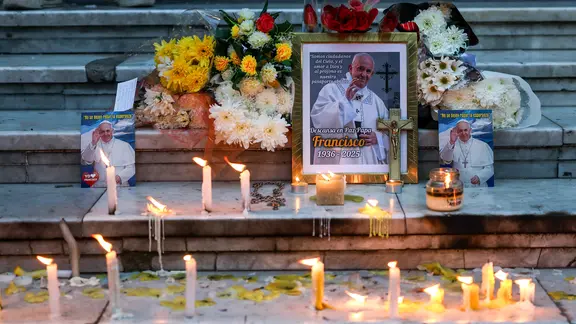 Auf Treppenstufen stehen ein Foto des gestorbenen Papst Franziskus, Blumen und brennende Kerzen