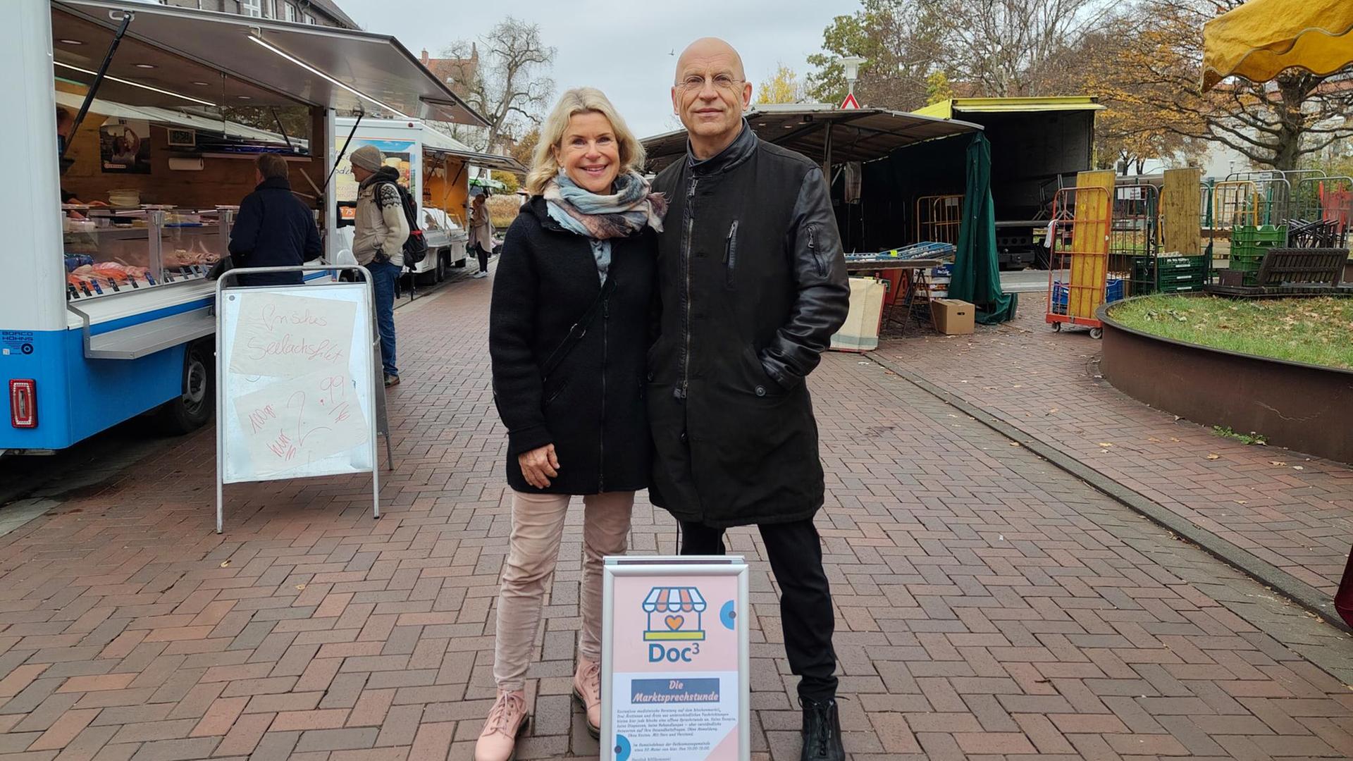 Auf einem Marktplatz stehen eine Ärztin und ein Arzt zur Sprechstunde bereit. | NDR/ Svenja Estner