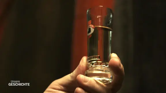 Eine Hand hält ein gefülltes Schnaps-Glas.