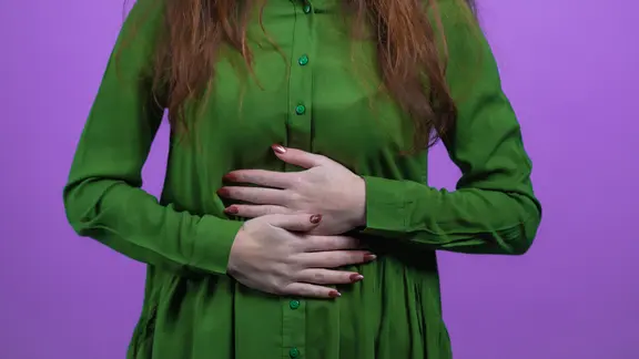 Eine Frau in Bluse hält sich mit beiden Händen den Bauch