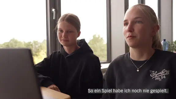 Zwei junge Schülerinnen sitzen an einem Tisch vor einem PC, direkt am Fenster.