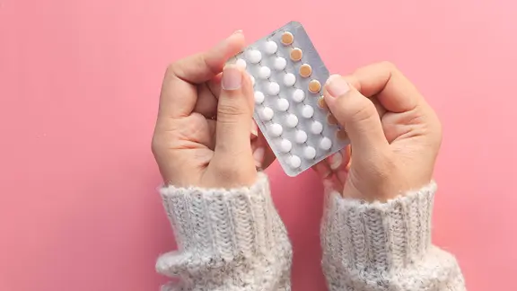 Frauenhände vor einem rosa Hintergrund. Sie halten ein Blister Antibabypille.