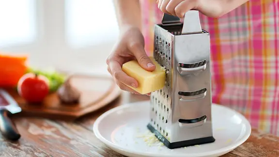 Käse wird mit Einsatz einer Käsereibe gerieben.