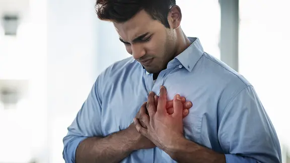 Kaliummangel: Mann hält mit verzerrtem Gesicht Hände an seine Brust