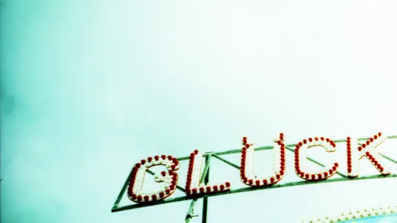 Zu sehen ist eine Leuchtreklame des Schriftzugs "Glück" vor blauem Himmel.