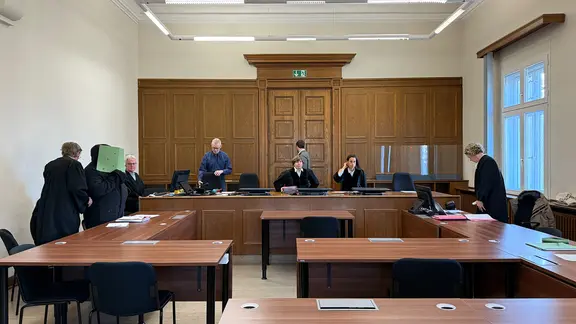 Der Beschuldigte steht im Gerichtsaal und verdeckt sein Gesicht.