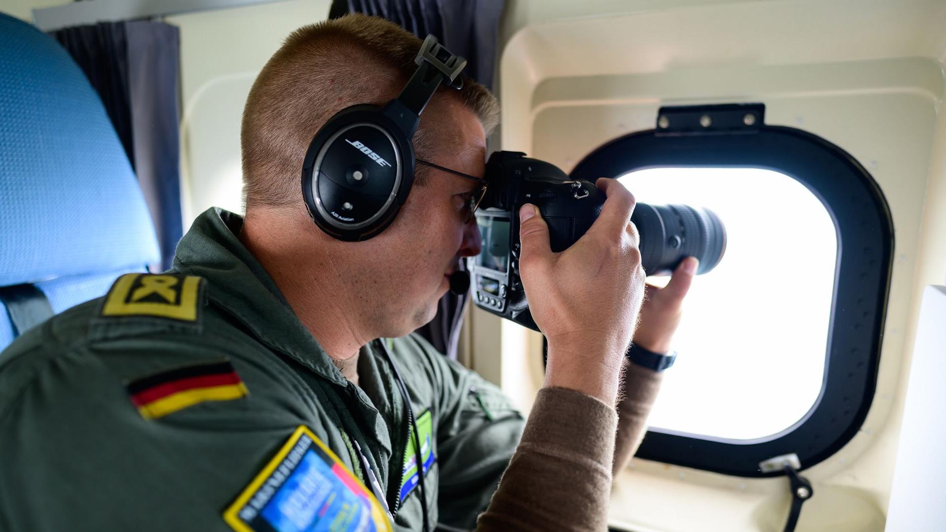 Ein Mann in Uniform dokumentiert aus einem Überwachungsflugzeug ein Schiff mit einer Kamera. | dpa, Philipp Schulze
