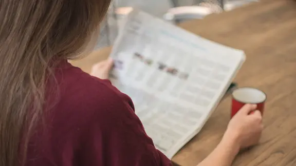 Blick über die Schulter eines Menschen auf eine Zeitung