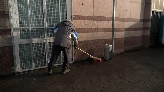 Ein Mann der Obdachlosen- und Drogenszene benutzt einen Besen zum Putzen.