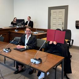 Eine Angeklagte sitzt im Gerichtssaal in Hamburg und verdeckt ihr Gesicht mit einer roten Mappe.