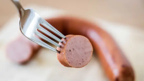 Ein Stück einer geräucherten Wurst ist auf einer Gabel aufgespießt. Im Hintergrund unscharf der Rest des Würstchens. | picture alliance / ANP | - Ein Stück einer geräucherten Wurst ist auf einer Gabel aufgespießt. Im Hintergrund unscharf der Rest des Würstchens.