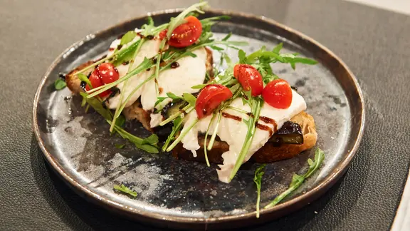 Bruschetta mit gegrillter Aubergine und Büffel-Mozzarella auf einem Teller serviert.