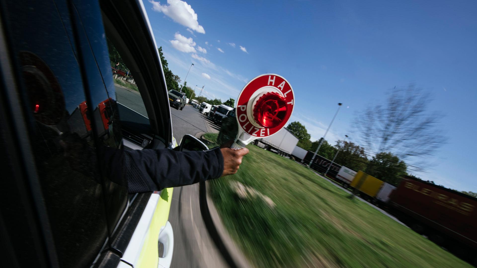 Ein Polizist streckt während der Fahrt einen Anhaltestab aus dem Einsatzwagen. | NDR, Julius Matuschik