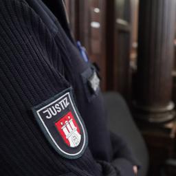 Die Rechtsanwälte stehen vor den angeklagten Frauen im Sitzungssaal im Strafjustizgebäude zu Beginn des Prozesses gegen eine Familie des mutmaßlichen Drahtziehers bei Schüssen auf ein Rockergang-Mitglied. Im Vordergrund ist ein Arm eines Justizbeamten zu sehen.