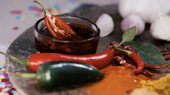 Chilischoten, Currypulver und Knoblauchzehen sind auf einem Tisch dekoriert, daneben liegt buntes Konfetti. | NDR, Oliver Zydek/Moritz Schwarz Chilischoten, Currypulver und Knoblauchzehen sind auf einem Tisch dekoriert, daneben liegt buntes Konfetti.