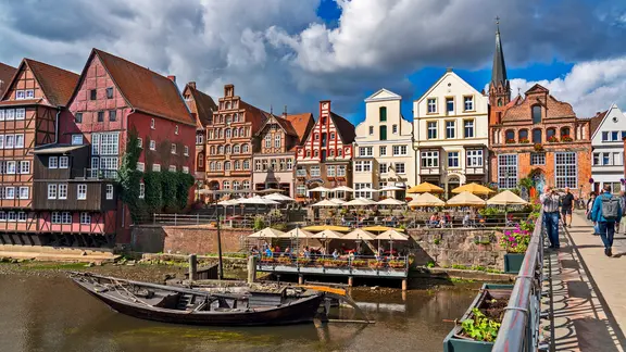 Rund um das historische Hafenviertel am Stintmarkt befinden sich heute zahlreiche Restaurants. | picture alliance , Jochen Tack Gebäude am Wasser und ein altes Boot am Lüneburger Stintmarkt