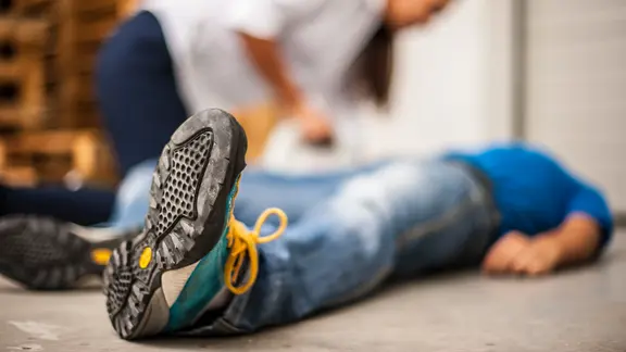 Im Notfall ist schnelle Hilfe wichtig. | pixelaway / photocase.de, pixelaway / photocase.de Eine Frau leistet einem bewusstlosen Mann, der auf dem Boden liegt, Erste Hilfe.