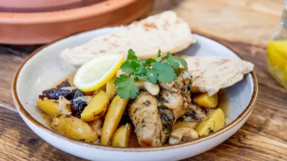 Tajine mit Huhn und ein Stück Brot auf einem Teller serviert.