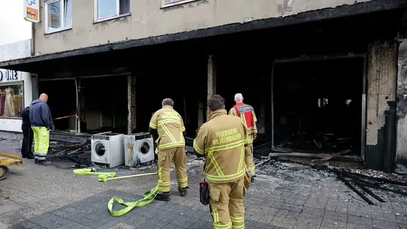 Feuerwehrleute stehen vor einem ausgebrannten Erdgeschoss eines Gebäudes in Wilhelmshaven.
