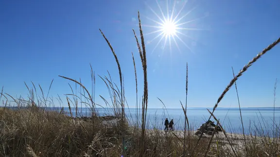 Neustadt in Holstein: Zwei Spaziergänger sind bei strahlendem Sonnenschein am Ostseestrand unterwegs.