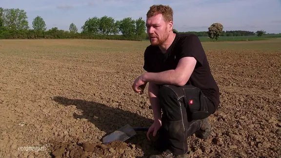 Ein Landwirt kniet auf einem trockenen Acker.