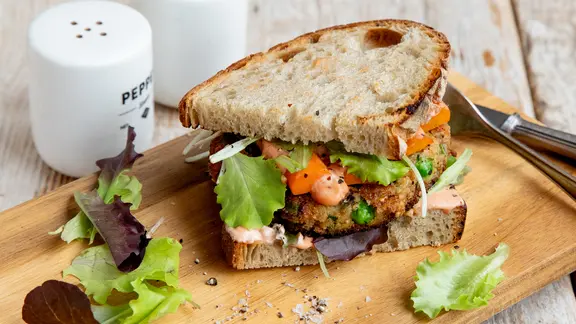 Ein vegetarischer Burger mit Suaerteigbrotscheiben liegt auf einem Holzbrett.