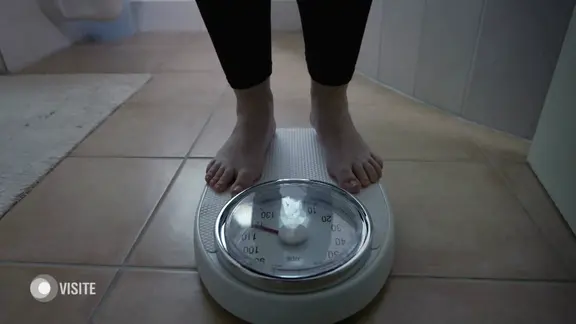 Man sieht die Füße einer Person, die auf einer Waage steht.