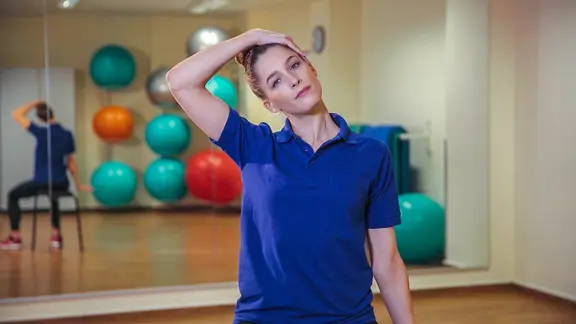 Svea Köhlmoos zieht ihren Kopf mit dem rechten Arm seitlich Richtung rechte Schulter.