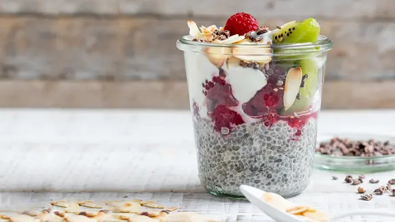 Auf dem Tisch steht ein Glas Chia-Pudding, mit Obst verziert.