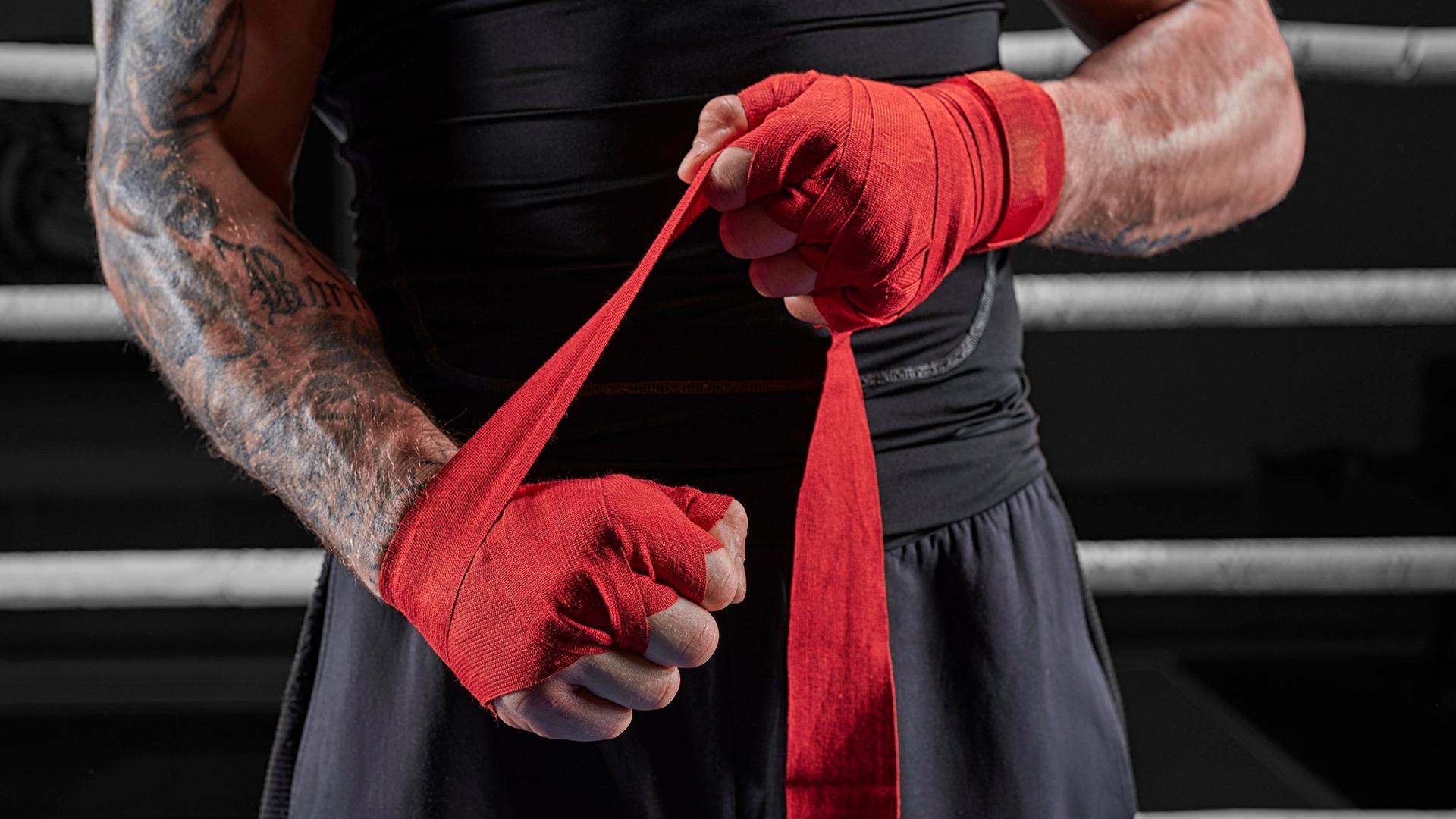 Ein Kickboxer bindet sich im Ring rote Bandagen an die Hände. | picture alliance/imageBROKER, Andy Gin