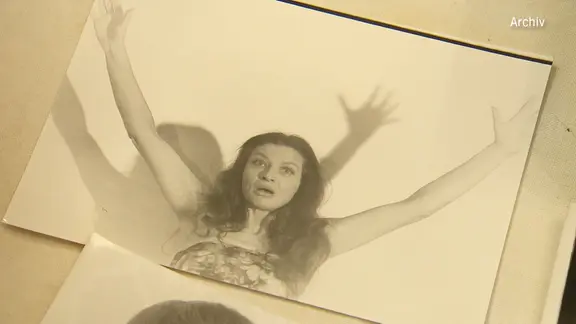 Die Schwarz-Weiß-Fotografie einer jungen Frau mit hochgesteckten Armen und überraschtem Gesichtsausdruck. Es ist Schauspielerin Brigitte Antonius.