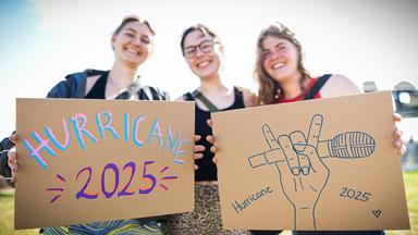 Festivalbesucherinnen Amelie (l-r), Amelie und Fenja stehen auf dem Gelände vom Hurricane Festival und halten selbstgemalte Pappschilder in die Kamera.